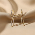SVORA gold-tone stainless steel dangle earrings with a ribbon knot design and clear cubic zirconia accents.