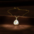 SVORA pendant necklace with a pearl drop, featuring a pink rose and green leaves design. Gold chain.