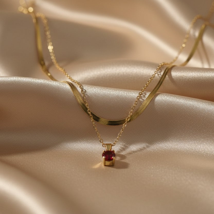 SVORA layered gold necklace with a ruby red stone pendant and snake chain detail.