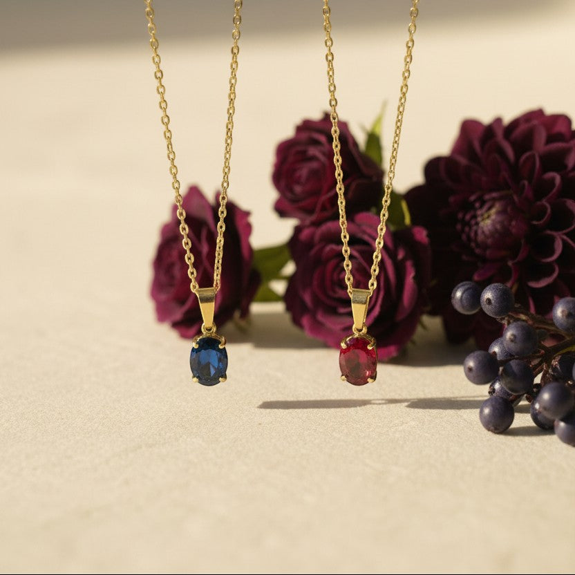 SVORA gold plated stainless steel necklace with a ruby red oval crystal pendant. Layered snake and fine link chains.