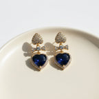 SVORA gold tone earrings with sapphire blue crystal heart drops and pavé bow connectors.