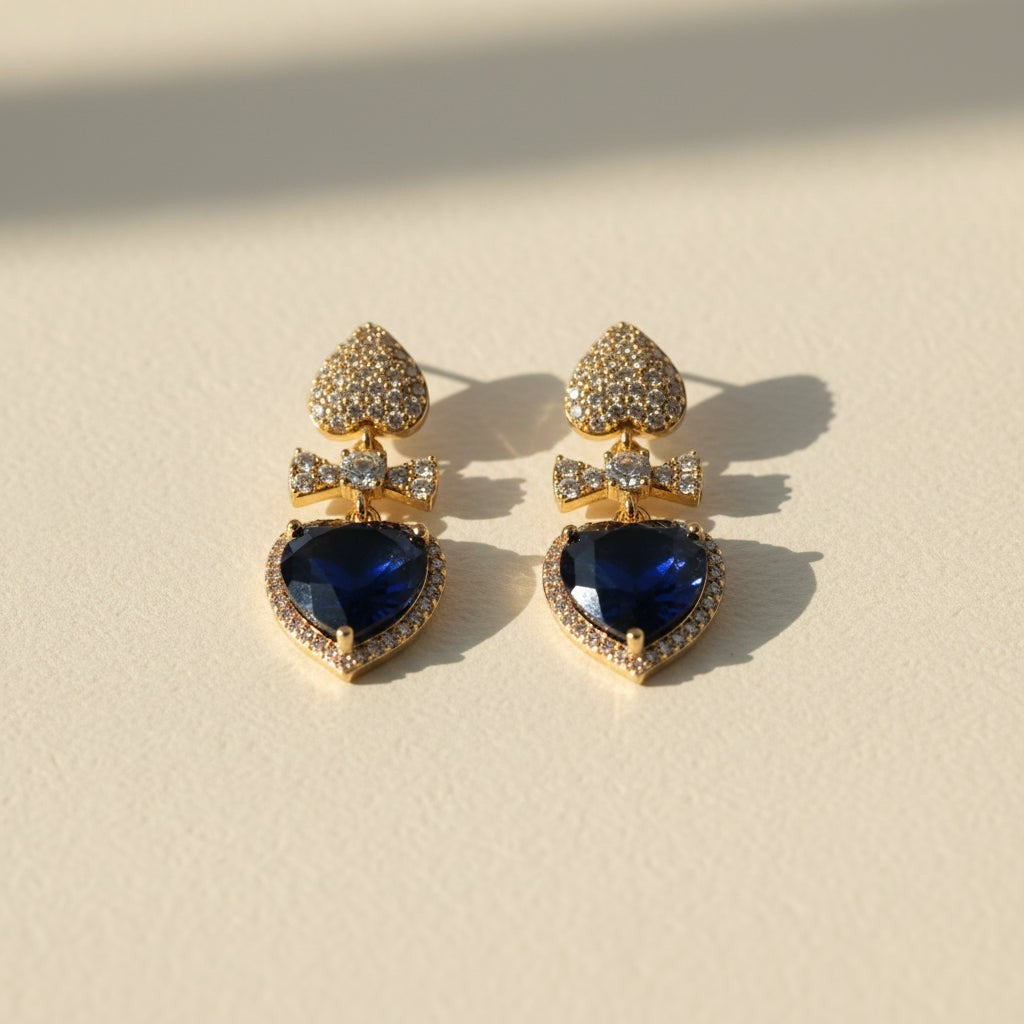 SVORA gold tone drop earrings with sapphire blue crystal hearts and pavé bow connectors.