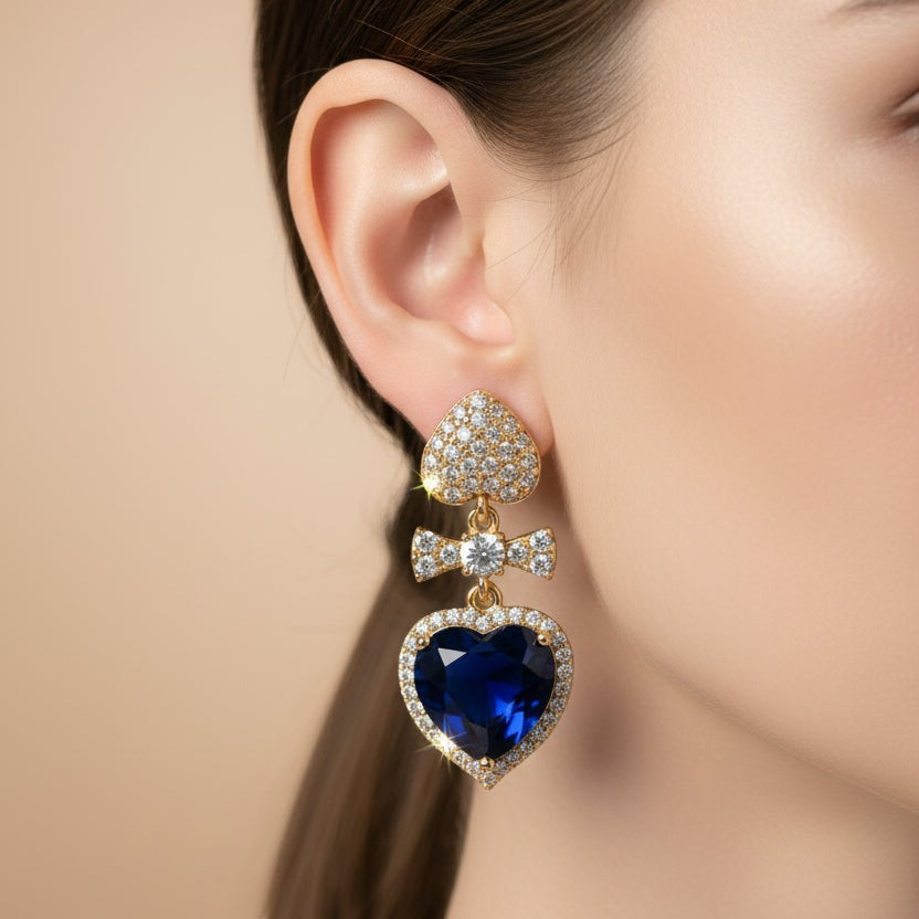 SVORA gold tone earrings with pavé heart stud, bow connector, and sapphire blue crystal heart drop.