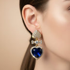 SVORA gold tone earrings with pavé heart stud, bow connector, and sapphire blue crystal heart drop.