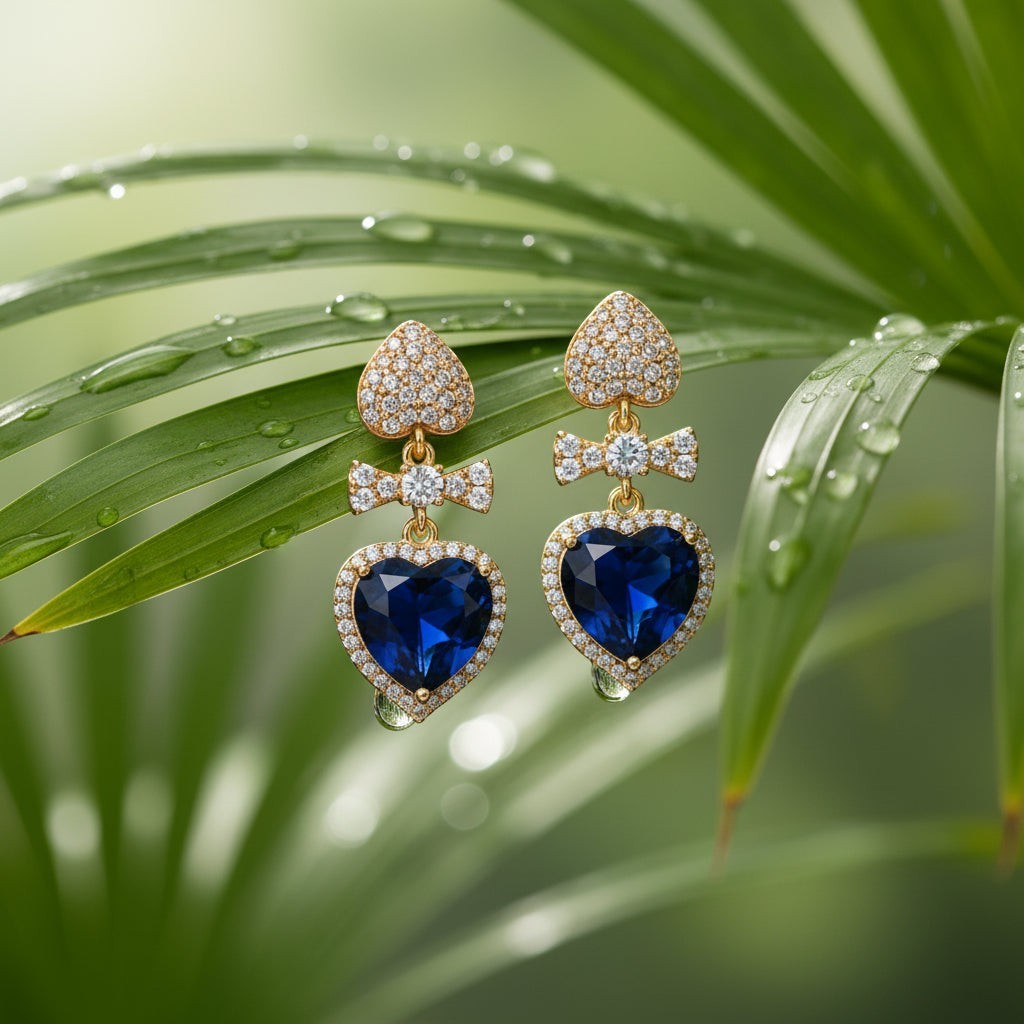 SVORA gold tone earrings with sapphire blue crystal heart drops and pavé bow connectors.