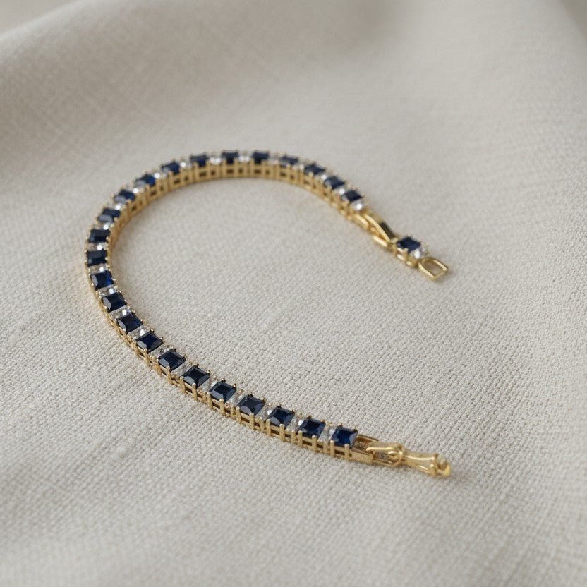 SVORA adjustable tennis bracelet with alternating sapphire blue and clear square-cut stones, set in gold-tone stainless steel.