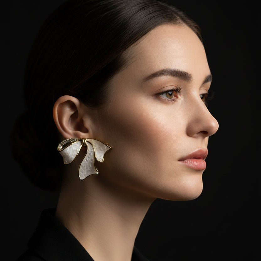 SVORA sculptural gold ribbon earrings with white inlay and pavé accents, designed for statement wear.