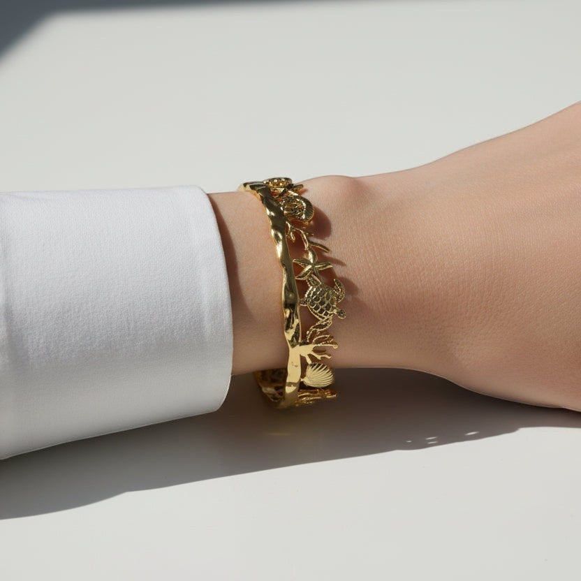 SVORA gold plated stainless steel cuff bracelet with sculpted palm, shell, turtle, and coral details.