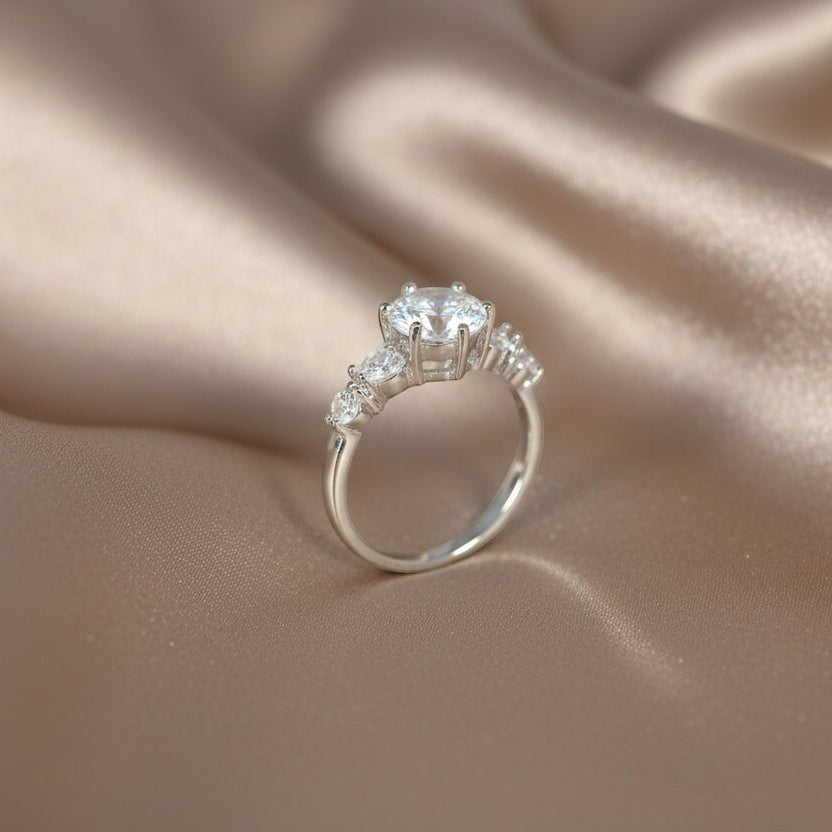 SVORA Ethereal Amour Solitaire Ring with clear round-brilliant center stone and heart-cut accent stones on rhodium-plated stainless steel band.