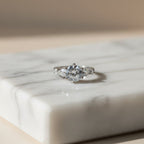 SVORA Ethereal Amour Solitaire Ring with round-brilliant center stone and heart-cut accent stones, rhodium-plated stainless steel.
