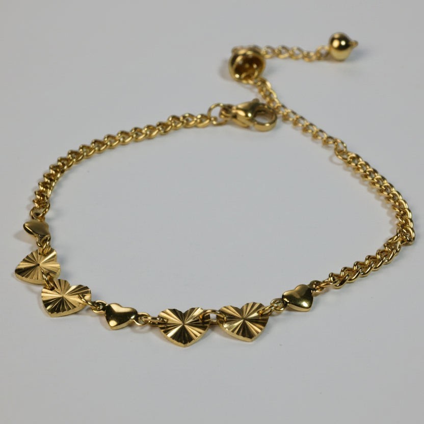 SVORA gold curb chain bracelet with seven heart charms, four textured and three solid. Adjustable lobster clasp.