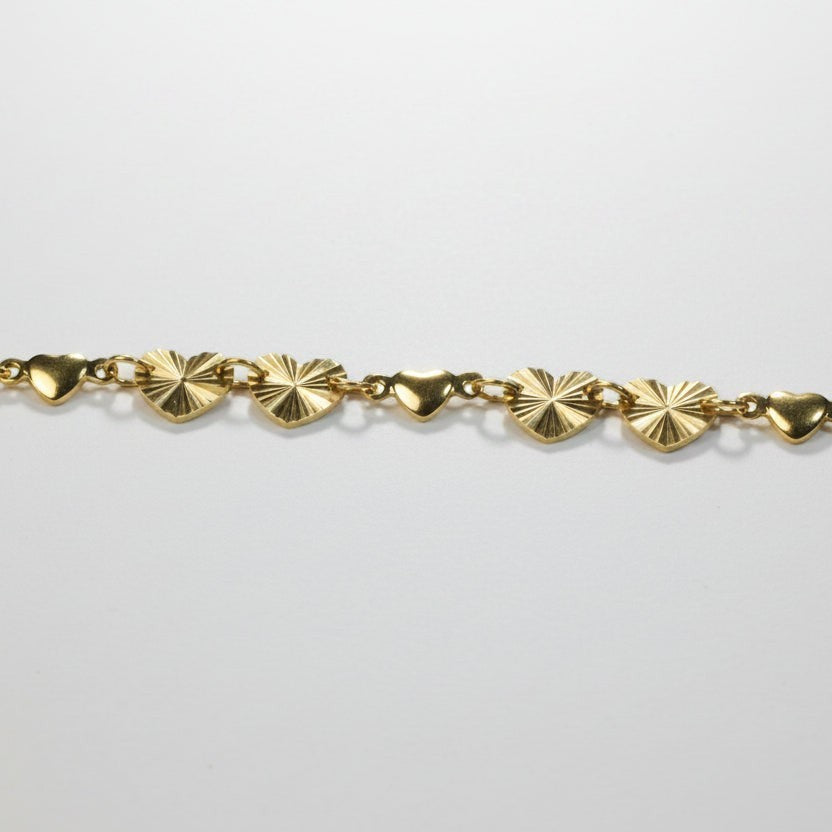 SVORA gold curb chain bracelet with seven heart charms, four textured and three solid. Adjustable with lobster clasp.