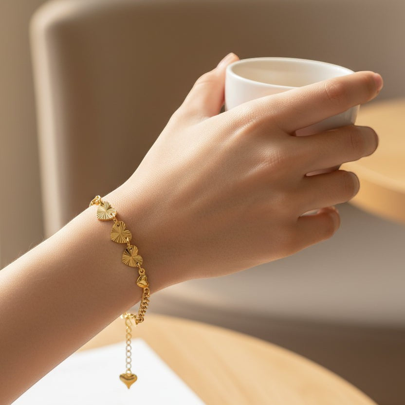 SVORA gold curb chain bracelet with seven heart charms, four textured and three solid, and a dangling heart charm.