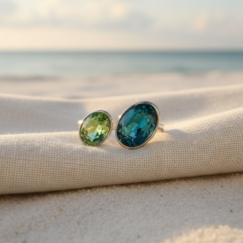 SVORA Toi et Moi ring with oval sapphire and emerald stones on a beach setting.