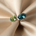 SVORA Toi et Moi ring with oval sapphire blue and emerald green stones on rhodium-plated stainless steel band.