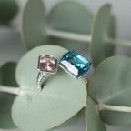 SVORA Toi et Moi Twilight Sapphire Ring with blue and pink stones on a ribbed silver band, set against eucalyptus leaves.