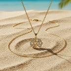 SVORA gold Tree of Life necklace with white CZ stones on a delicate chain, set on a sandy beach.