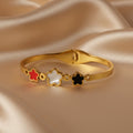 SVORA gold bracelet with three five-petal flower charms in red, white, and black. 18K gold plated stainless steel.