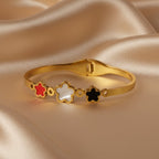 SVORA gold bracelet with three five-petal flower charms in red, white, and black. 18K gold plated stainless steel.