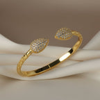 SVORA gold plated stainless steel cuff bracelet with pavé leaf ends and scaled band design.