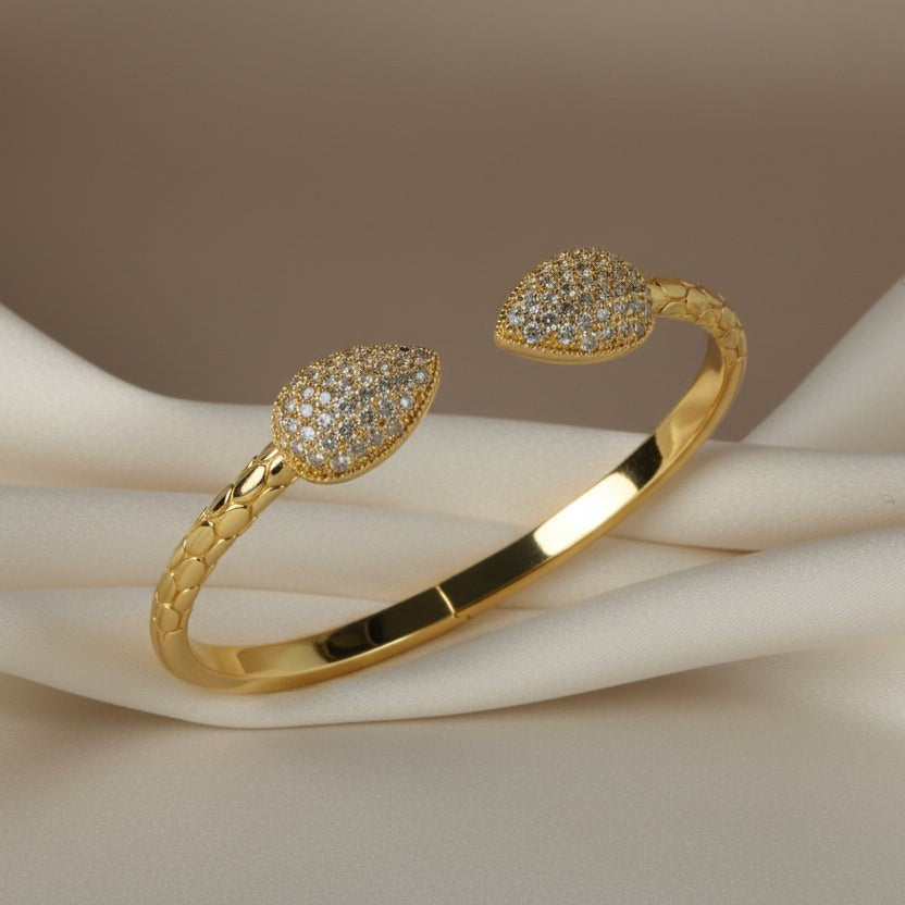 SVORA gold plated stainless steel cuff bracelet with pavé leaf ends and scaled band design.