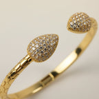 SVORA gold plated stainless steel cuff bracelet with pave leaf ends and scaled band. Cubic zirconia stones.
