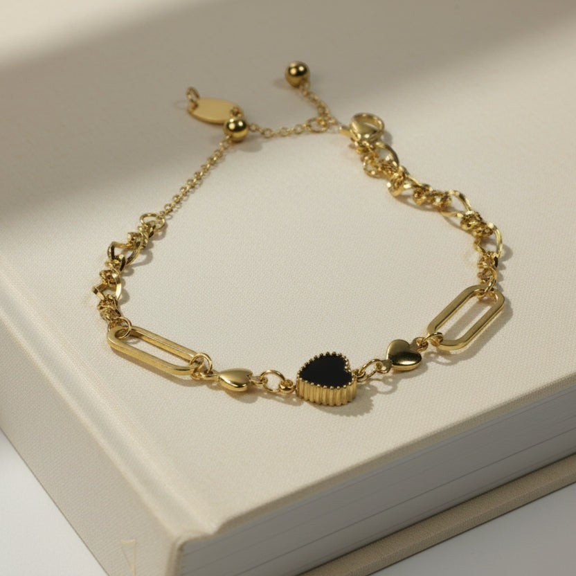 SVORA gold twisted rope chain bracelet with a black heart charm and smaller gold heart charms.
