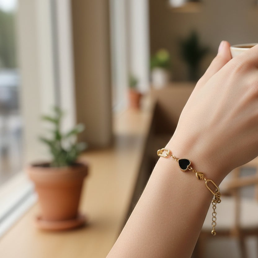 SVORA gold twisted rope chain bracelet with a black heart charm and two gold heart charms.