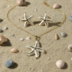 SVORA white pearlescent starfish necklace and earrings set with gold edges on a sandy beach.