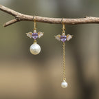 SVORA asymmetric gold-tone earrings with purple heart charms, wings, and pearl drops.