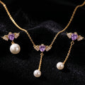 SVORA gold-tone necklace and asymmetric earrings with purple winged hearts and pearl drops.