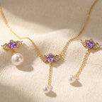 SVORA gold-tone necklace and asymmetric earrings with purple winged heart pendants and pearl drops.