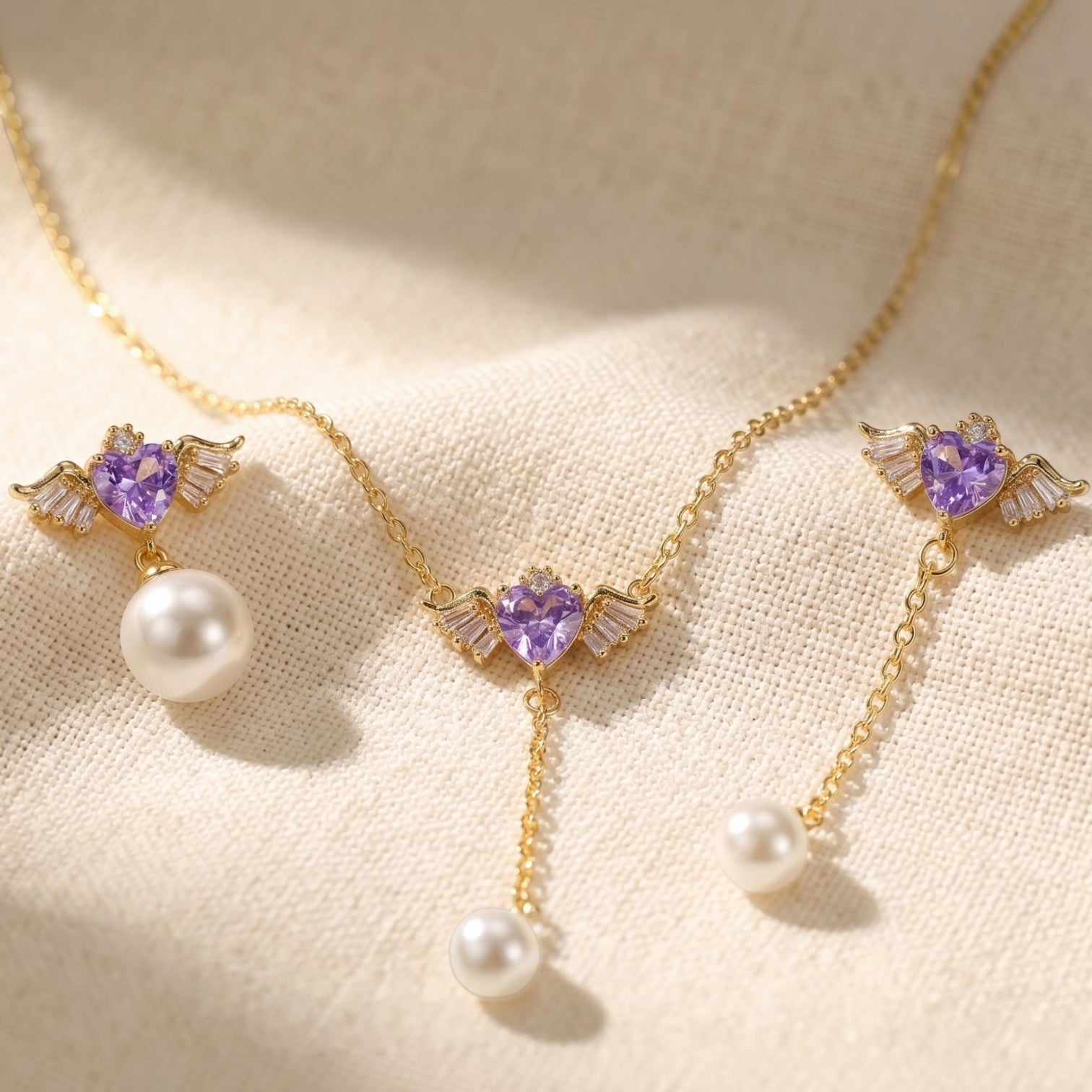 SVORA gold-tone necklace and asymmetric earrings with purple winged heart pendants and pearl drops.