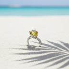 SVORA Ethereal Yellow Sapphire Solitaire Ring with pavé shoulders on a white sand beach.